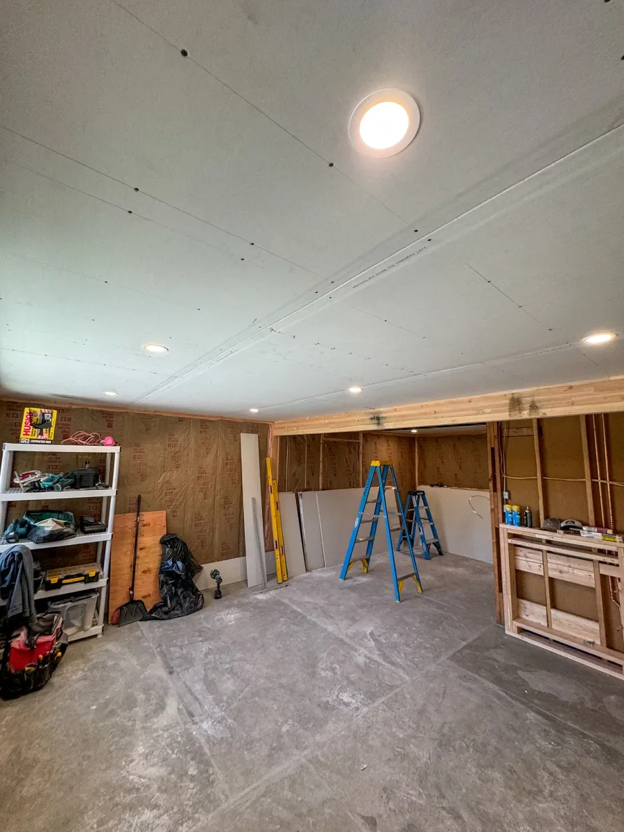 Basement remodel under construction with installed insulation and drywall sheets stacked against wall ready to be installed