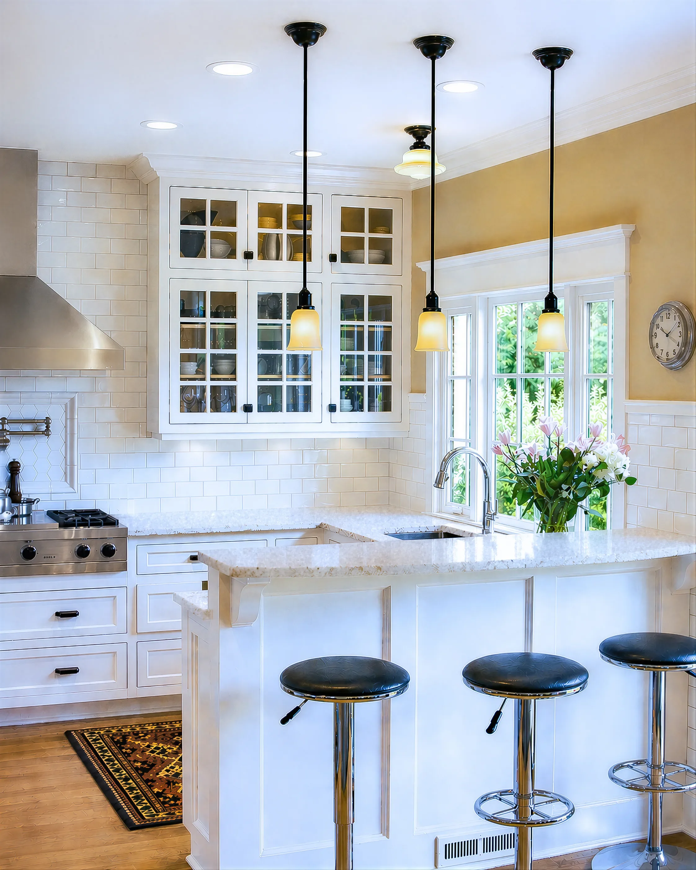 Tudor kitchen remodel in historic district Mapleton Hill in Boulder, CO featuring crowned custom glass display cabinets, stainless steel stove range with inset tile framed wall mounted pot filler, and multi-tiered counter with barstool seating