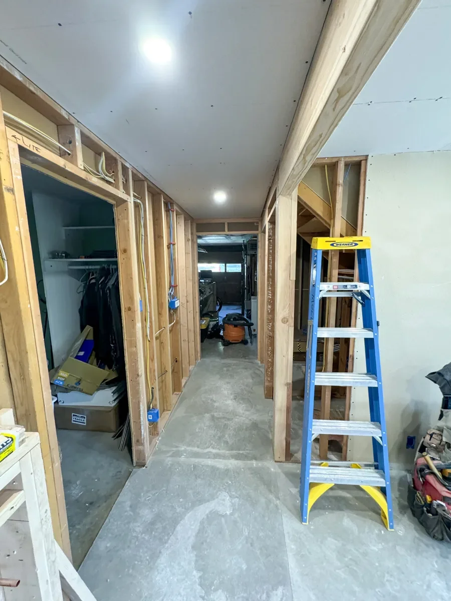 Unfinished hallway view of home remodel site with fresh framing, concrete floors, and unfinished drywall ceiling panels