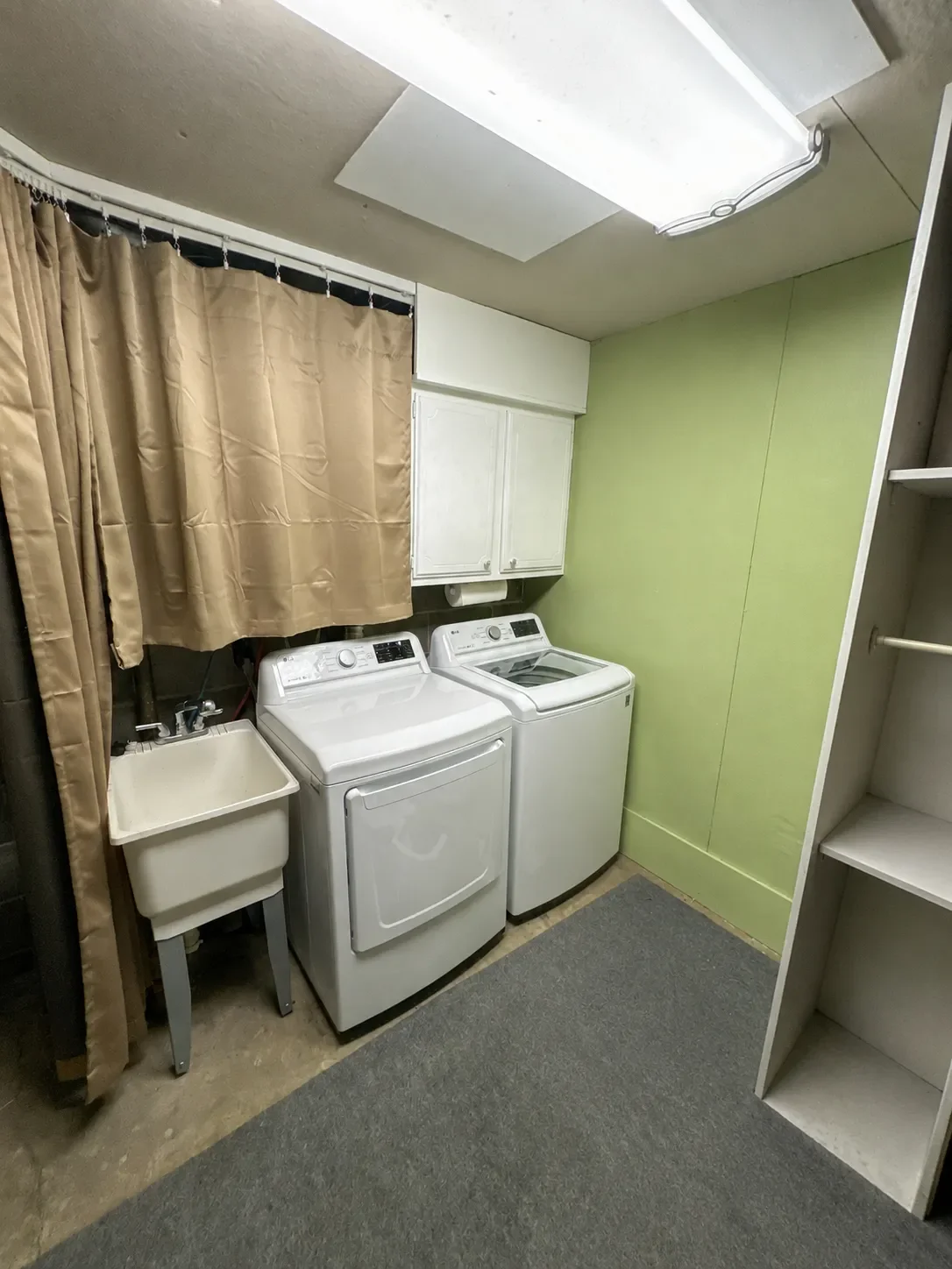 Utility and laundry room in unfinished basement prior to remodeling in Seven Hills, Boulder, CO with drop panel ceiling, concrete floors, curtain wall, and flourescent lighting