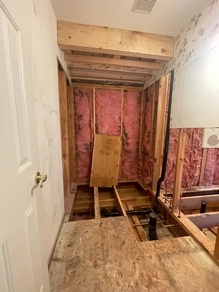 Gutted guest bathroom with exposed wall frame, insulation, and open floor with visible plumbing underneath in a Gunbarrel, CO home remodel in progress