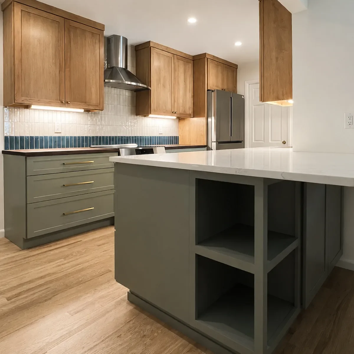Warm two-toned transitional mixed-material kitchen remodel in Longmont, CO featuring natural maple upper cabinets, sage green lower cabinets, white quartz and dark walnut countertops, and red oak hardwood floors