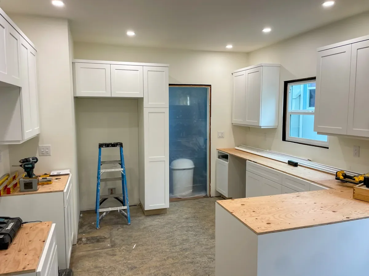 Kitchen under renovation in Lafayette, CO with white cabinets, plywood countertops, a ladder, unfinished floor, and construction tools.
