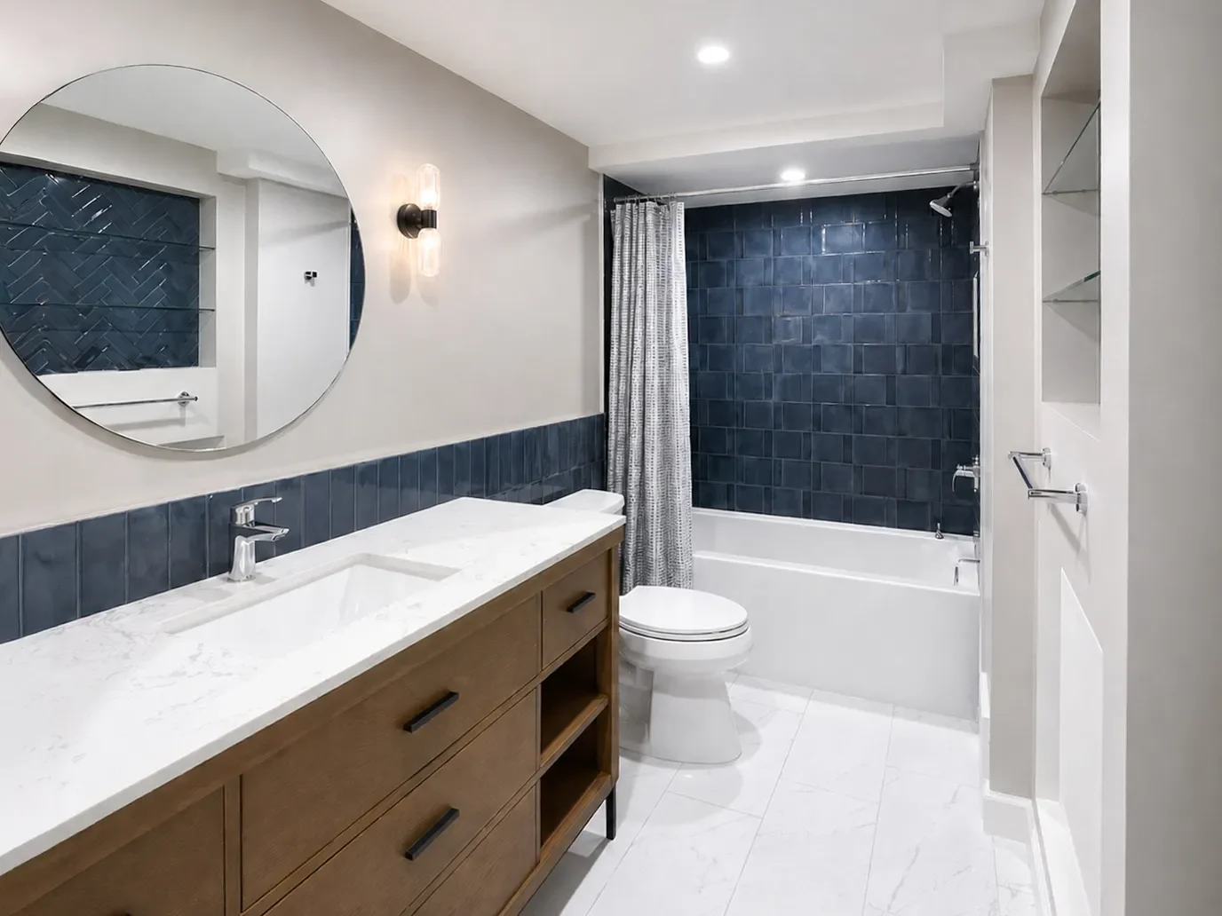 Contemporary bathroom remodel in Seven Hills, Boulder, CO featuring custom natural wood vanity, white marble floors, white marble countertops, large soaking tub, radiant heat, bold blue tile, and circular vanity mirror with LED wall sconces