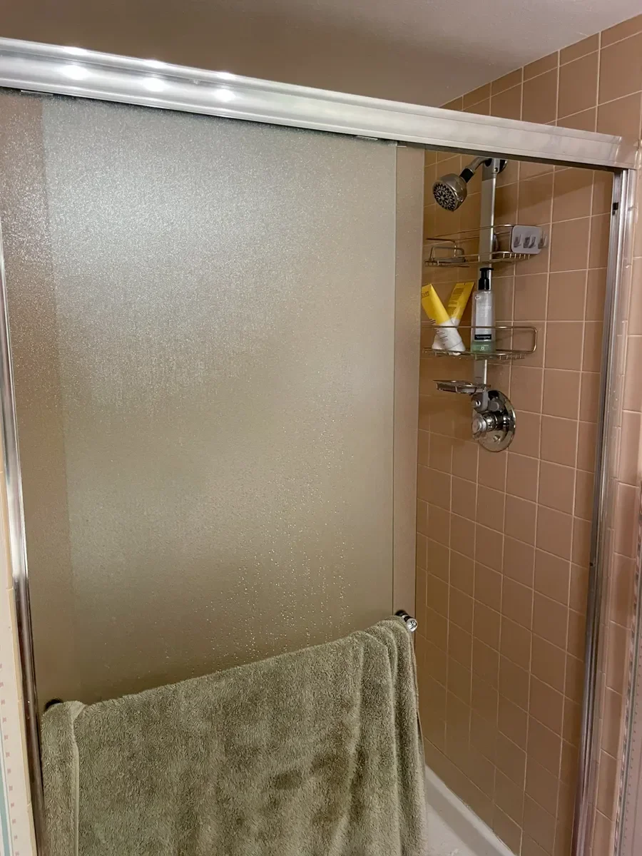 Niwot, CO dark basement bathroom remodel before picture featuring frosted glass shower door and 70's vintage brown tile color