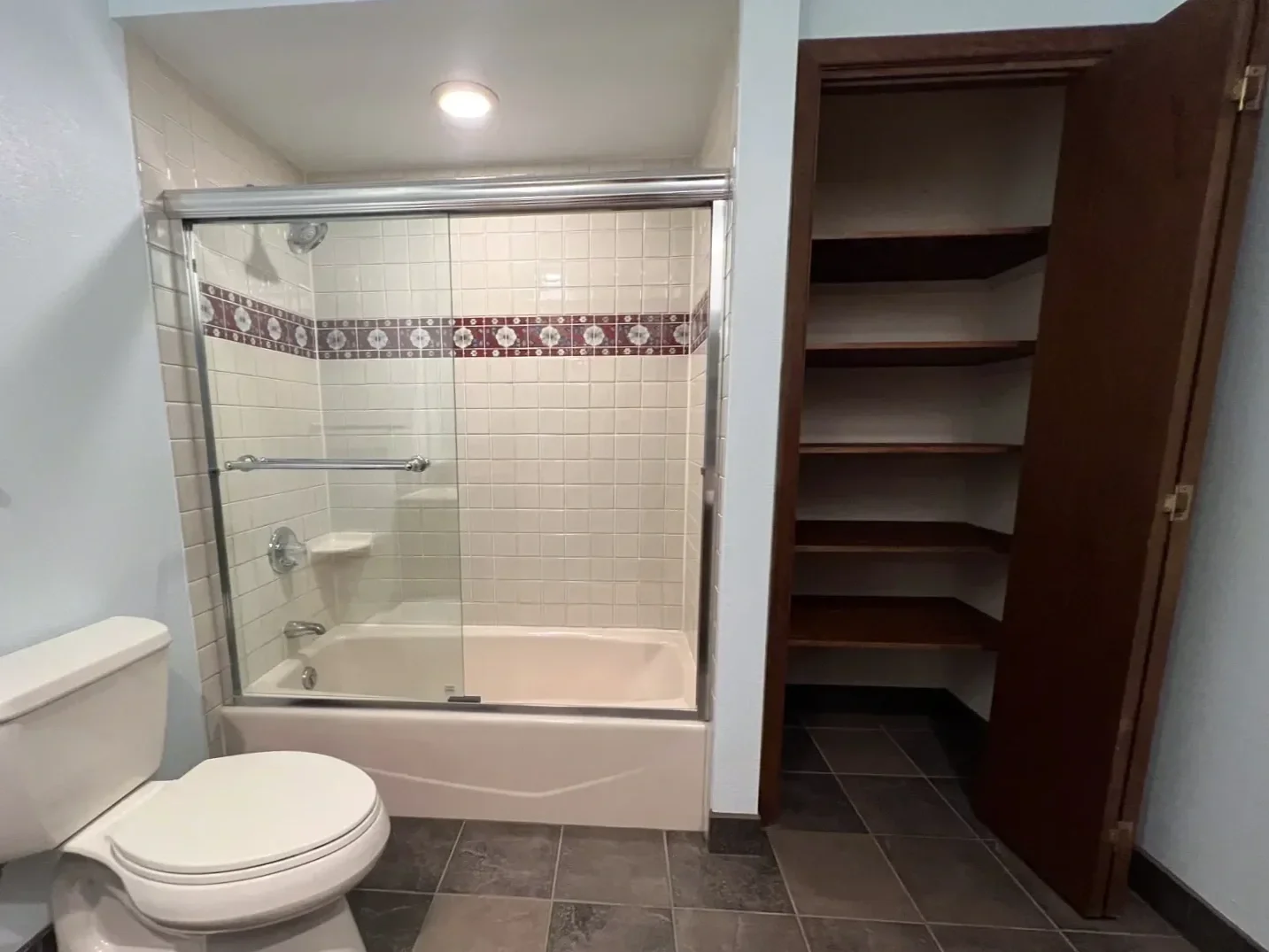 The before photo of a bathroom prior to remodeling, showing a dated bathtub with sliding glass shower door partition and enclosed linen closet made of dark wood. Shown beside a photo of the finished bathroom remodel.