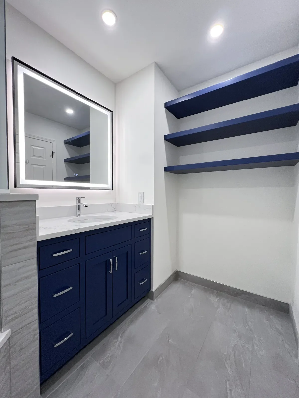 Reconfigured master bathroom layout after a remodel in Gunbarrel, CO with blue floating shelves and matching custom vanity along a wall that was formerly an entrance to a closet.