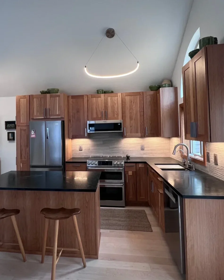 North Boulder, CO kitchen renovation featuring open layout, island barstool seating, cherry wood custom craftsman cabinets, ivory textured tile backsplash, and vaulted ceilings with contemporary LED ceiling pendant lights