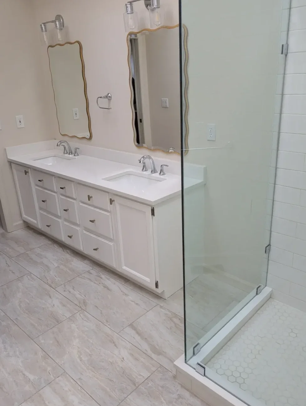 Dimly lit master bathroom in Gunbarrel, CO featuring white double vanity and basic glass walk-in shower, photo taken just before the start of the remodeling process