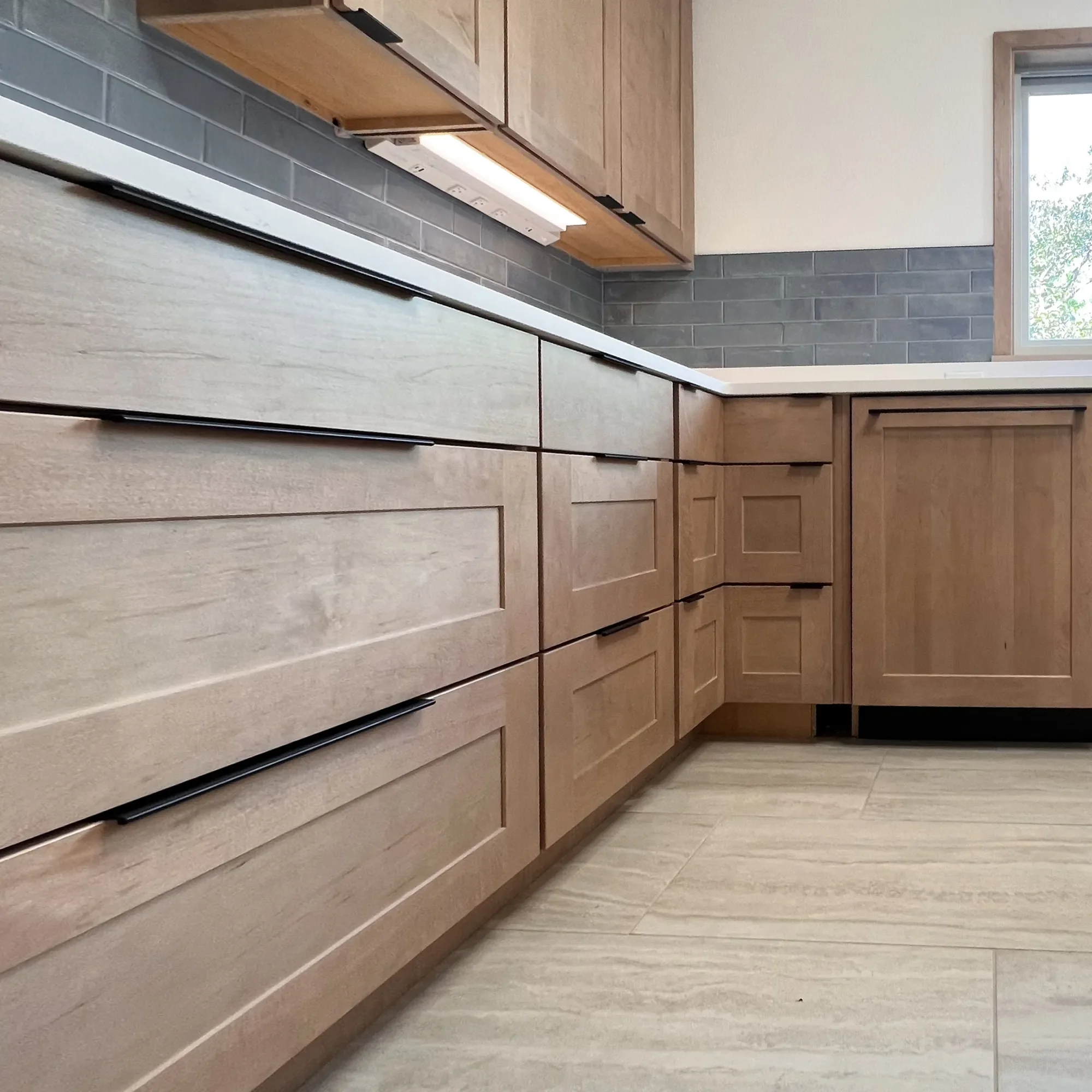 Close up detail of custom maple-stained white oak cabinet drawers with matte black drawer pulls and integrated appliance panels and blue subway tile backsplash in a North Boulder, CO contemporary craftsman kitchen remodel