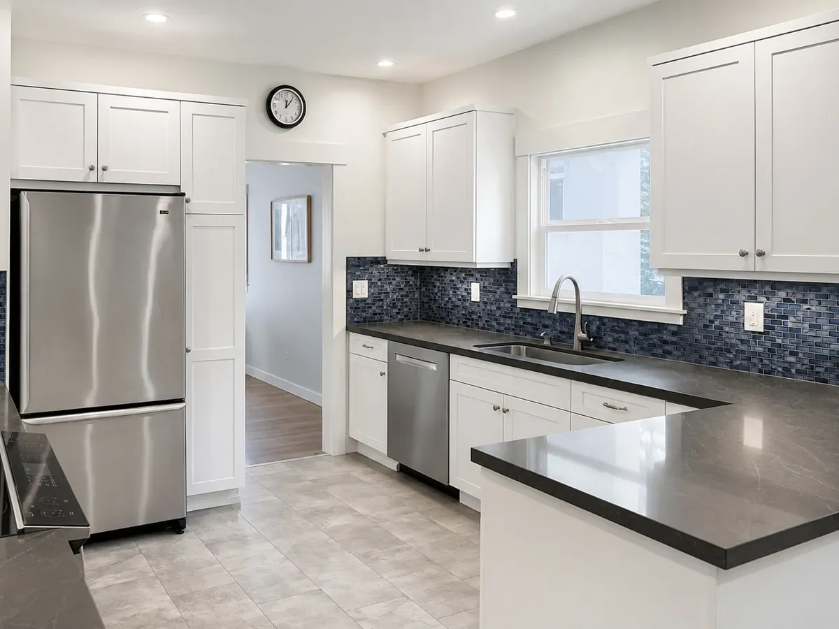Modern kitchen with white cabinets, stainless steel appliances, dark countertops, tile backsplash, recessed lighting, and a wall clock.