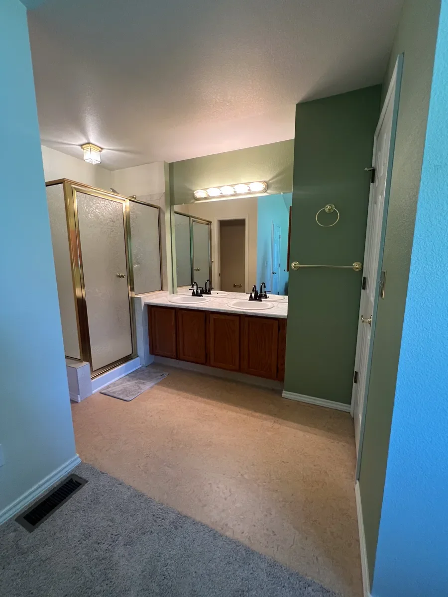 Master bathroom awaiting remodel in Gunbarrel, CO featuring laminate flooring, outdated shower and light fixtures, and a wide open doorway into master bedroom with lack of privacy