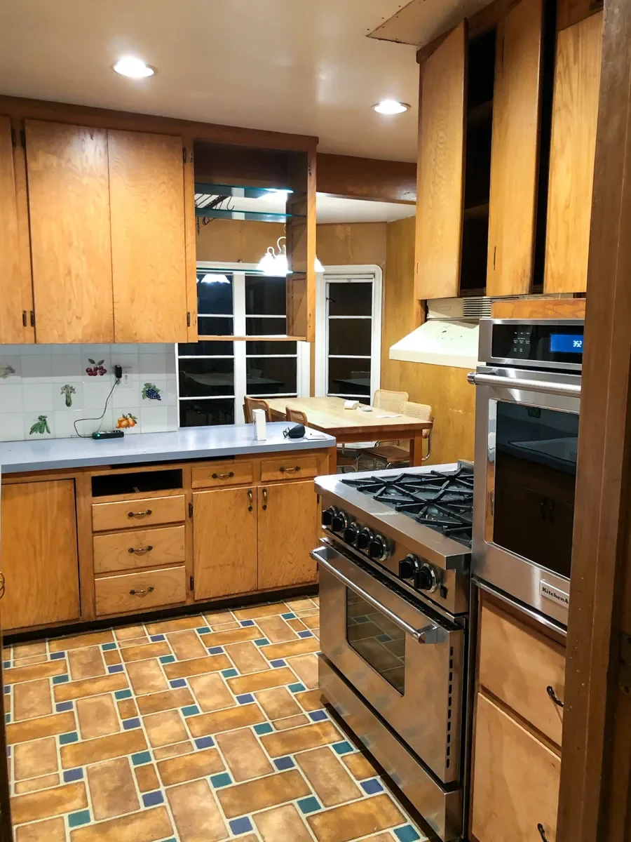 Retro kitchen before remodeling in Louisville, CO with wooden cabinets, tiled backsplash, gas stove, dishwasher, and mosaic tile flooring