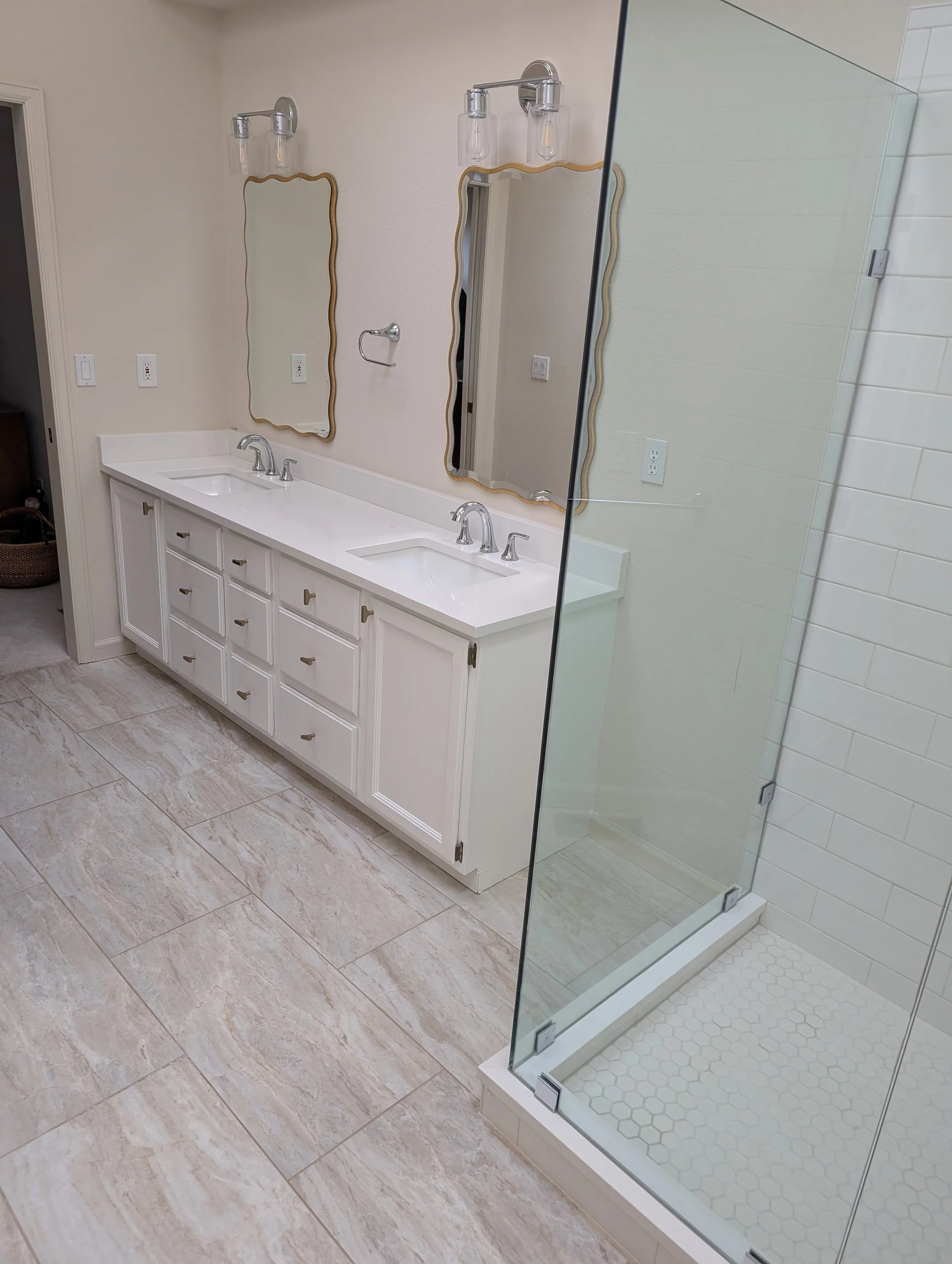 Master bathroom in Gunbarrel, CO before remodel, with small walk-in shower enclosed by glass, wasted floorplan space between white double vanity and enclosed shower, and lack of bathtub