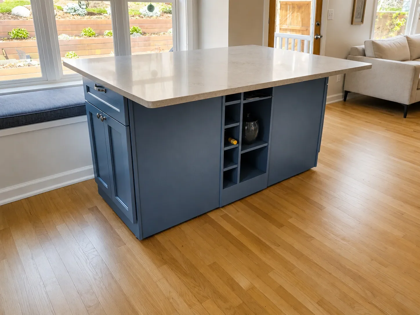 Blue custom handcrafted kitchen island on oak hardwood floors next to cushioned bay window breakfast nook seating with cut out shelving and additional kitchen cabinet storage in Superior, CO