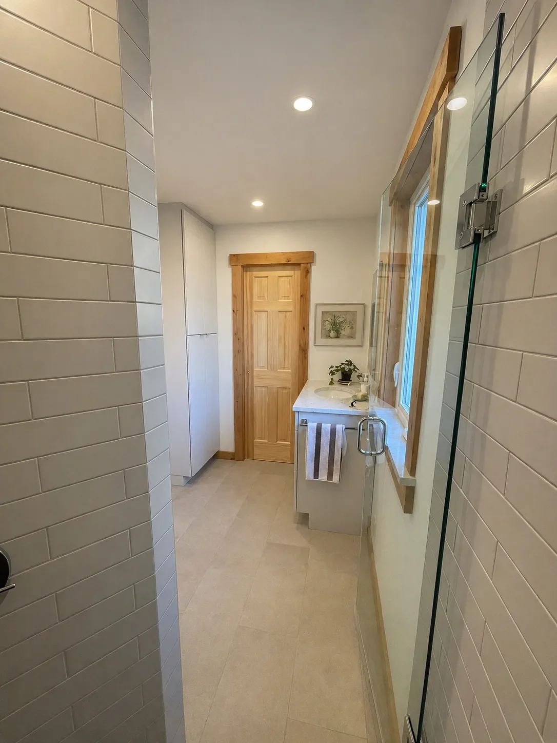 Pine Brook Hills remodeled modern rustic bathroom in Boulder, CO viewed from walk-in shower interior looking out at gray budget vanity, stone tile floors, and cedar trimmed door and window