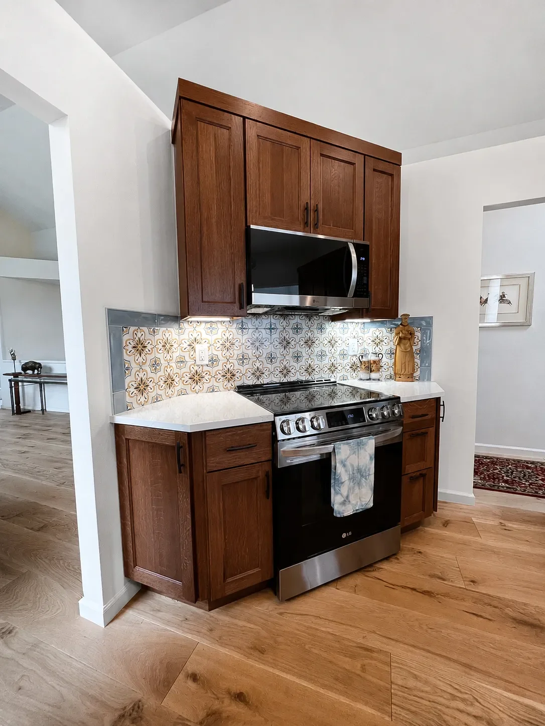 Remodeled contemporary craftsman kitchen in Gunbarrel, CO  featuring custom walnut stained crowned cabinetry framing stainless steel induction range stove and microwave with patterned blue and gold tile backsplash