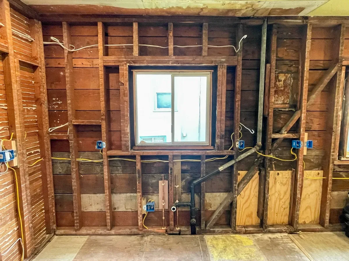 Room under renovation with exposed wooden wall studs and electrical wiring around a square double paned sliding window