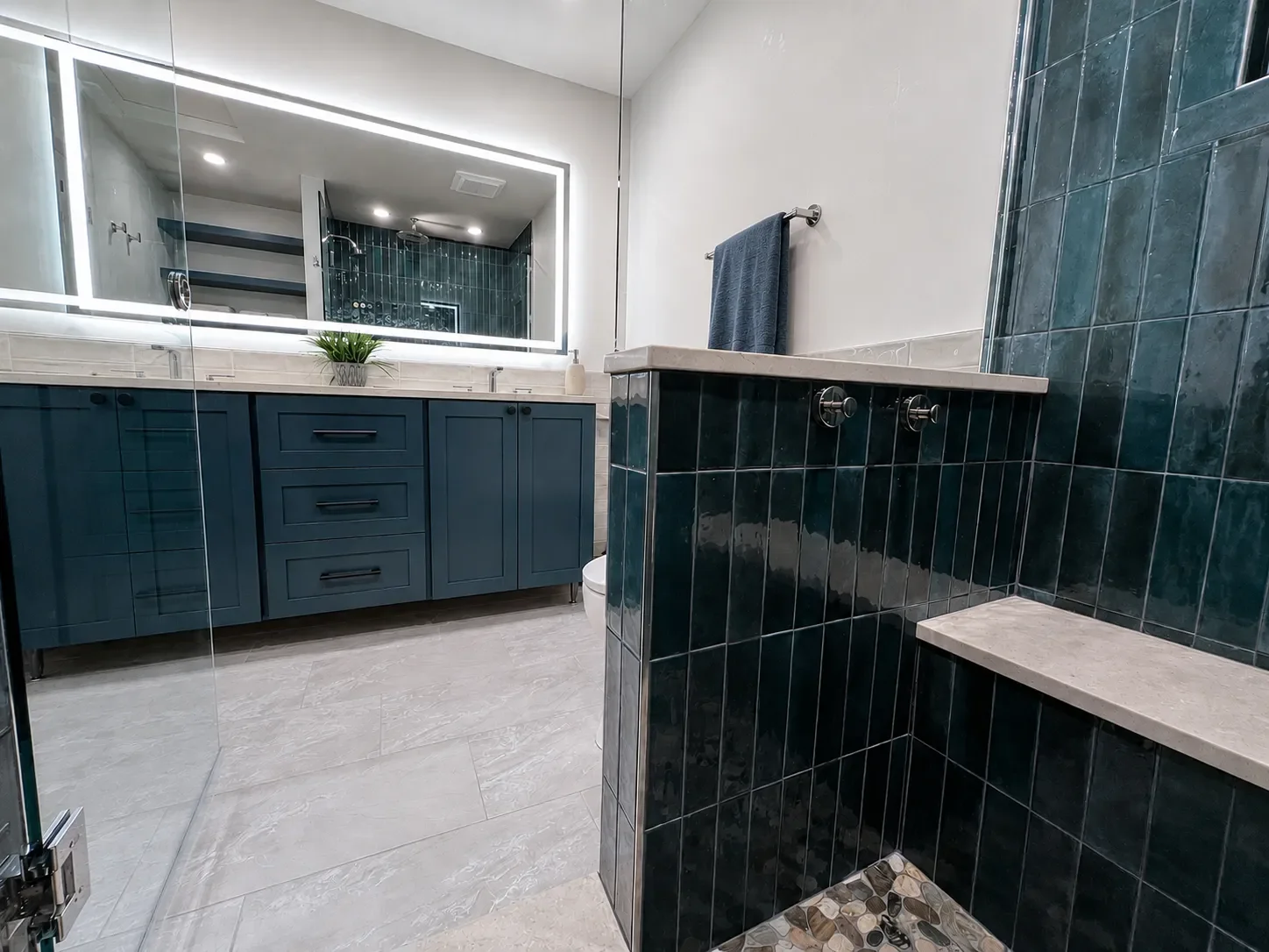 Contemporary spa bathroom remodel with bold teal soldiered shower tile, shower bench, and custom blue shaker vanity with large rectangular LED mirror