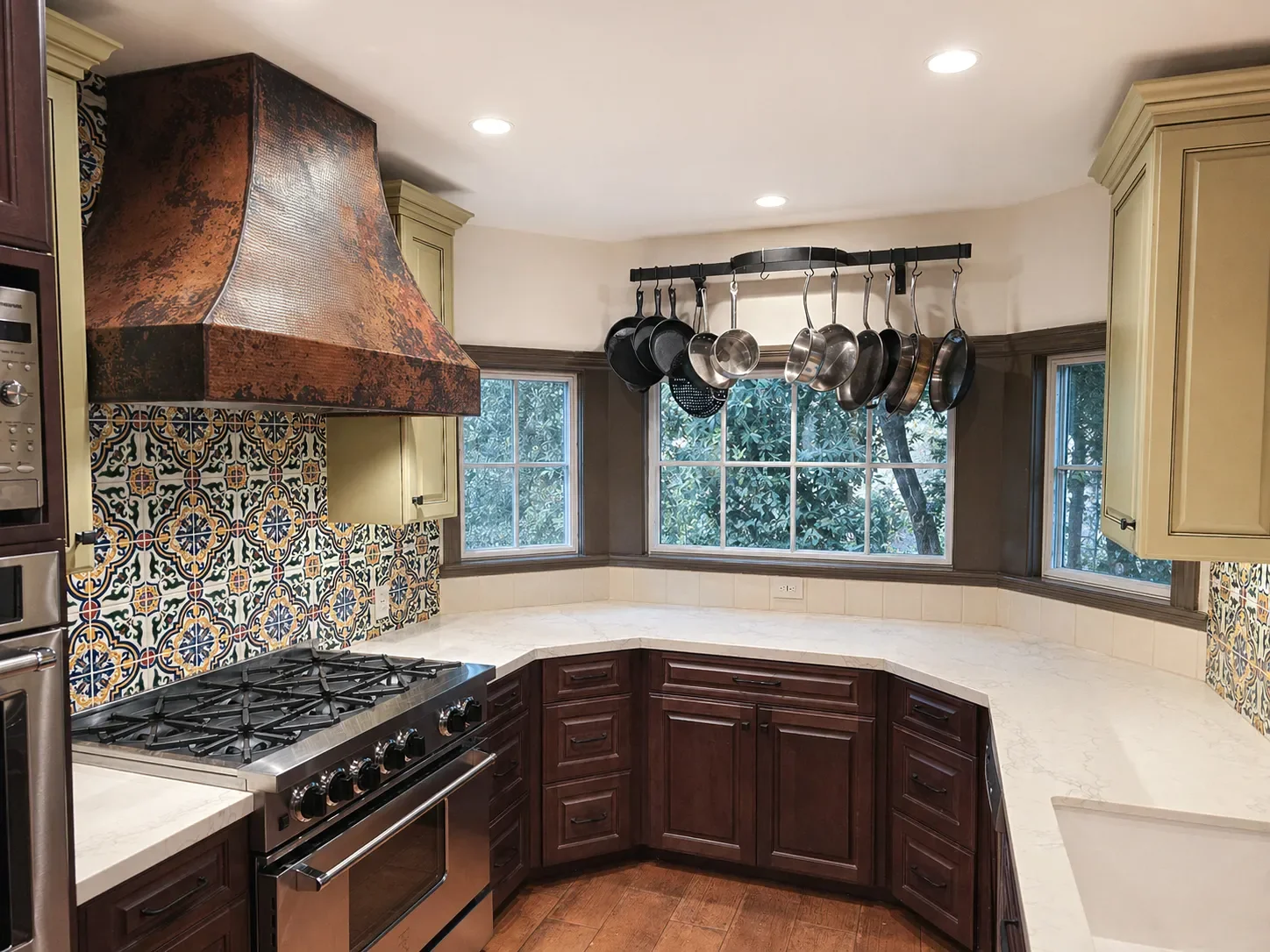 Modern kitchen with dark wood cabinets, stainless steel appliances, and a patterned tile backsplash. Brightly lit with recessed lights and featuring a view of a patio through glass doors.