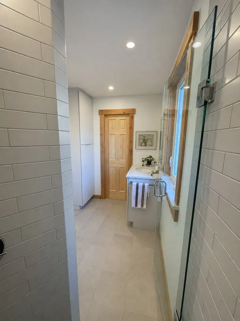 View from inside frameless glass door walk-in shower with gray subway shower tile looking out at rustic, minimal bathroom remodel with gray stone tile floors, matching vanity and storage cabinets, and cedar wood trim in a Boulder, CO bathroom remodel
