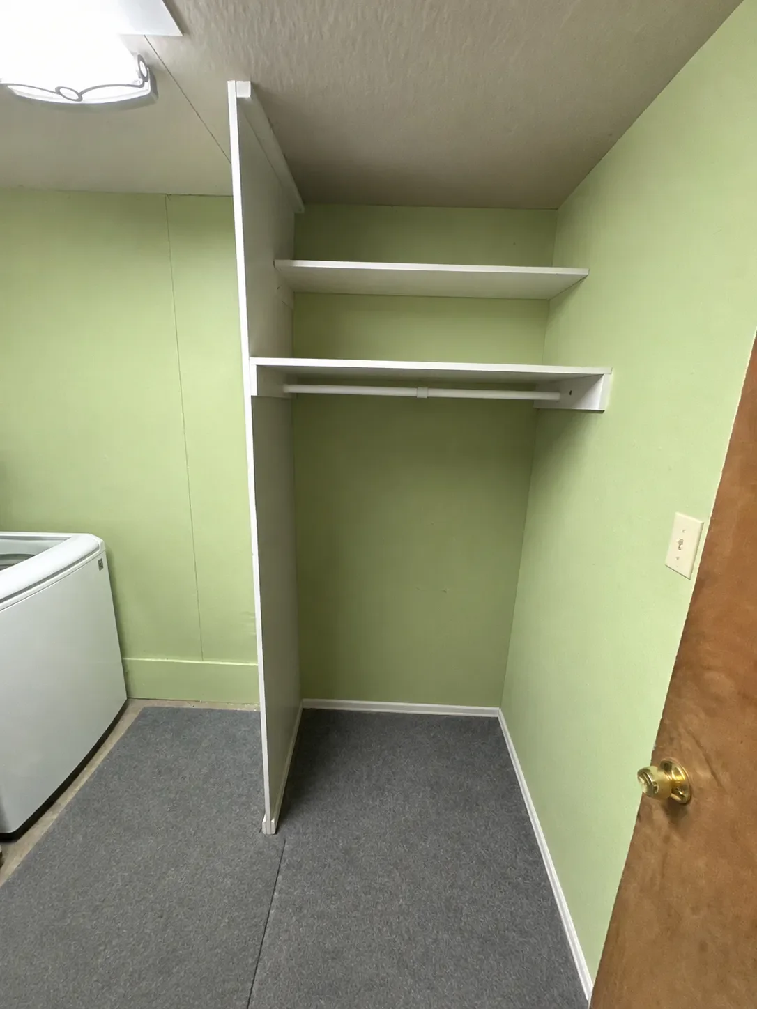Laundry room closet in an unfinished basement before being remodeled in Boulder, CO featuring particle board walls and shelving, flourescent overhead lighting, and unfinished concrete floors