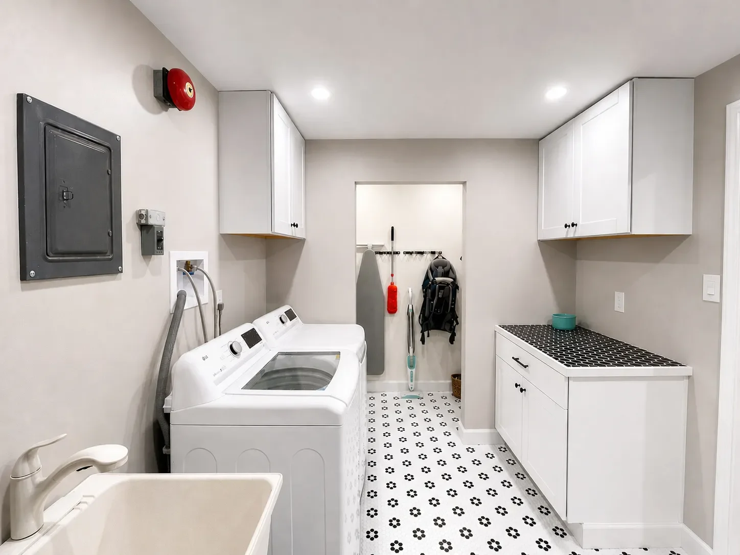 Modern laundry room with washer and dryer, utility sink, white cabinets, decorative tile floor, and wall-mounted storage hooks.