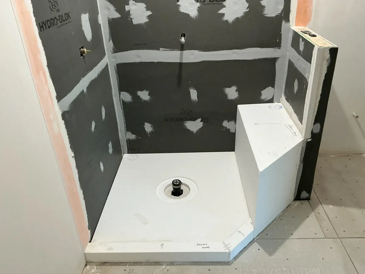 Newly installed shower floor pan with bench seating in an unfinished bathroom remodel in progress in Gunbarrel, CO