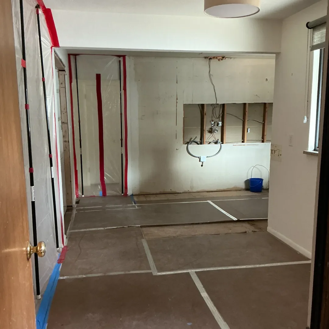 Kitchen in Longmont, CO in the process of being remodeled, immediately following demolition. Floors are protected and plastic dust protection barriers seal doorways. Drywall and electrical are exposed.