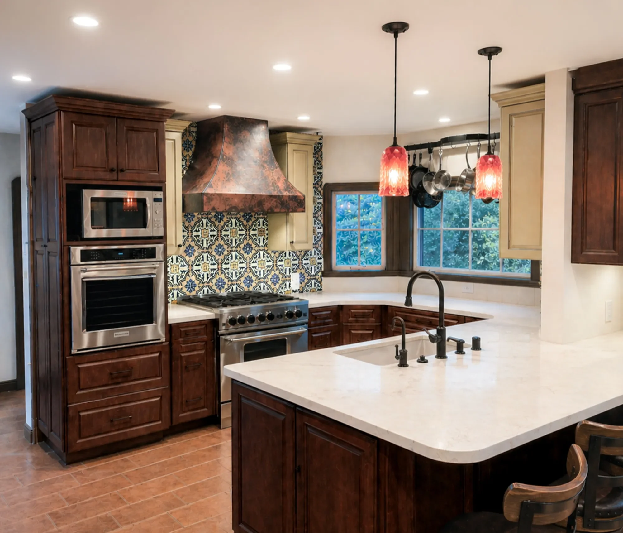 Old world mediterranean kitchen remodel in Louisville, CO with hand painted pattern tile backsplash, copper stove range hood, stainless steel appliances, and red handblown glass pendant lights