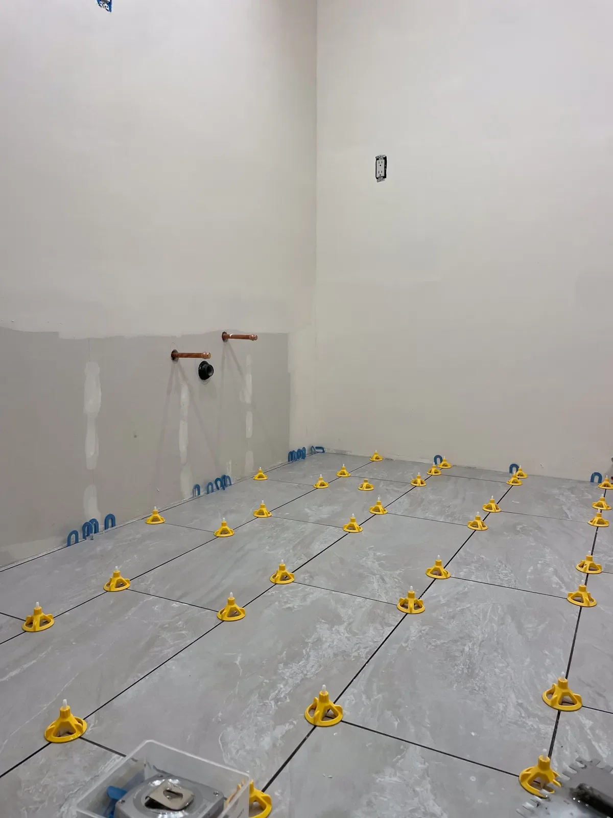 Newly laid floor tiles with spacers surrounded by unfinished drywall in a bathroom in the process of being remodeled in Boulder, CO