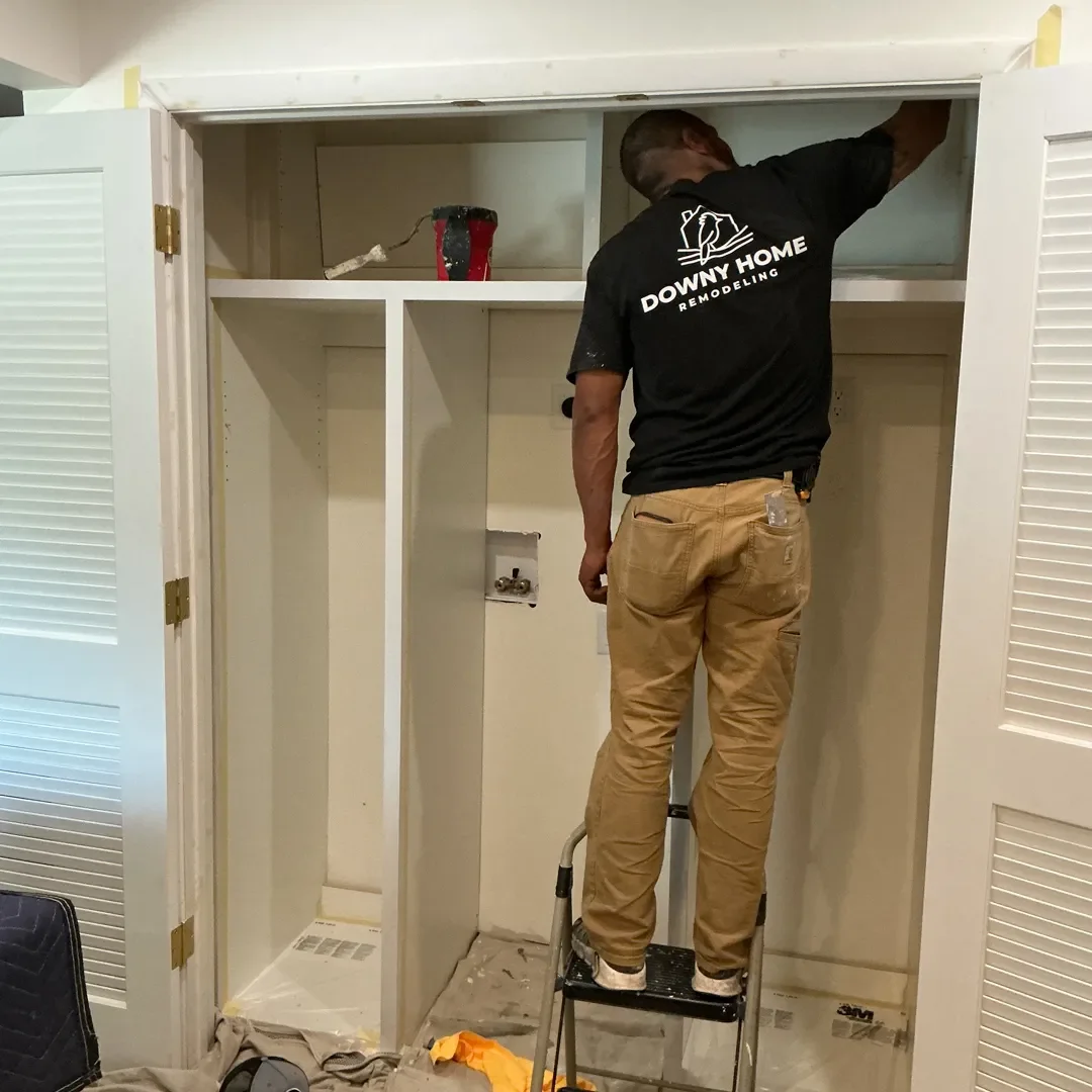 An employee of Downy Home Remodeling painting new custom shelving inside the laundry closet of a home being remodeled in Longmont, CO
