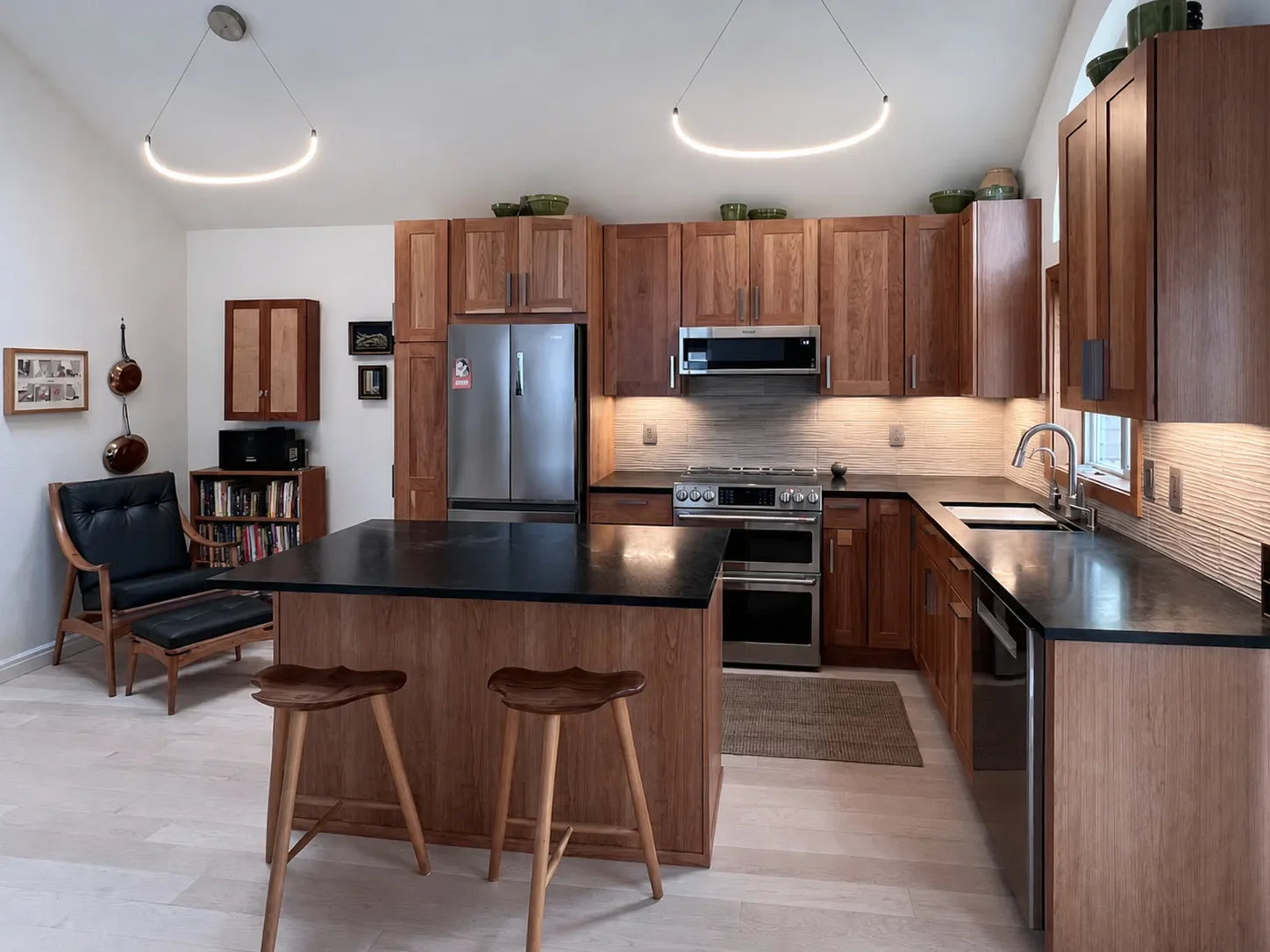 Remodeled townhouse kitchen in Newlands, North Boulder, CO featuring vaulted ceilings, open layout, custom cherry wood shaker style cabinets, textured tile backsplash, and dark green soapstone countertops with barstool island seating