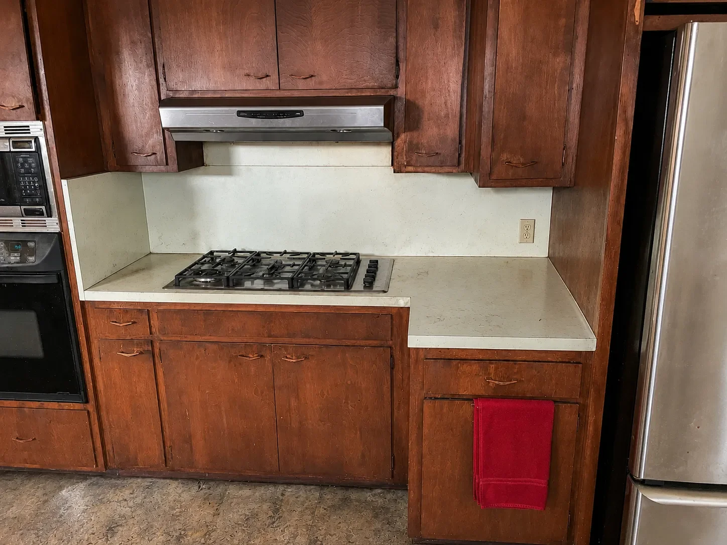 Vintage kitchen with damaged wooden cabinets, built-in oven, oxidized countertops, and dirty linoleum floors in Lafayette, CO kitchen before renovation