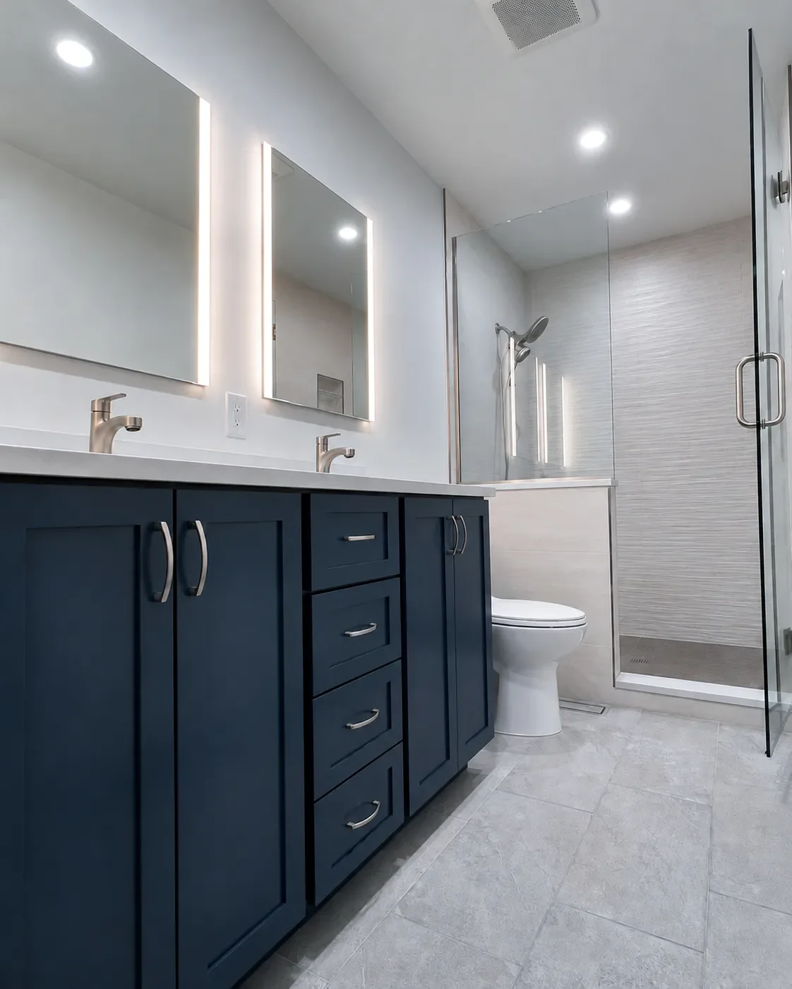 View of blue custom double vanity with recessed cabinet LED mirrors and walk-in shower with swinging glass door and privacy half wall in a completed contemporary bathroom remodel in Boulder, CO