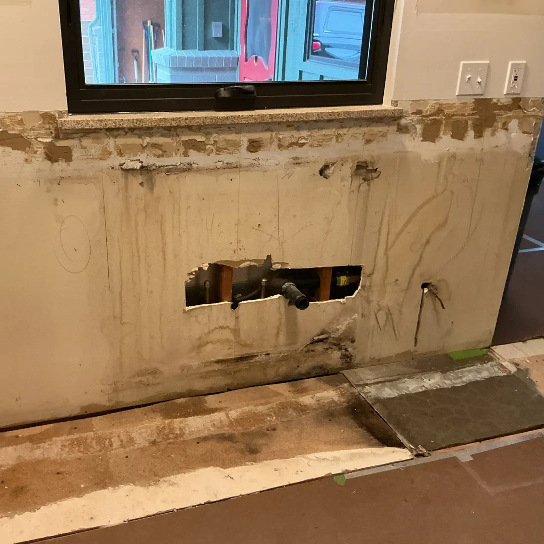 Kitchen remodel in progress in Longmont, CO featuring wall with water damage behind old kitchen sink following demolition, awaiting new drywall.