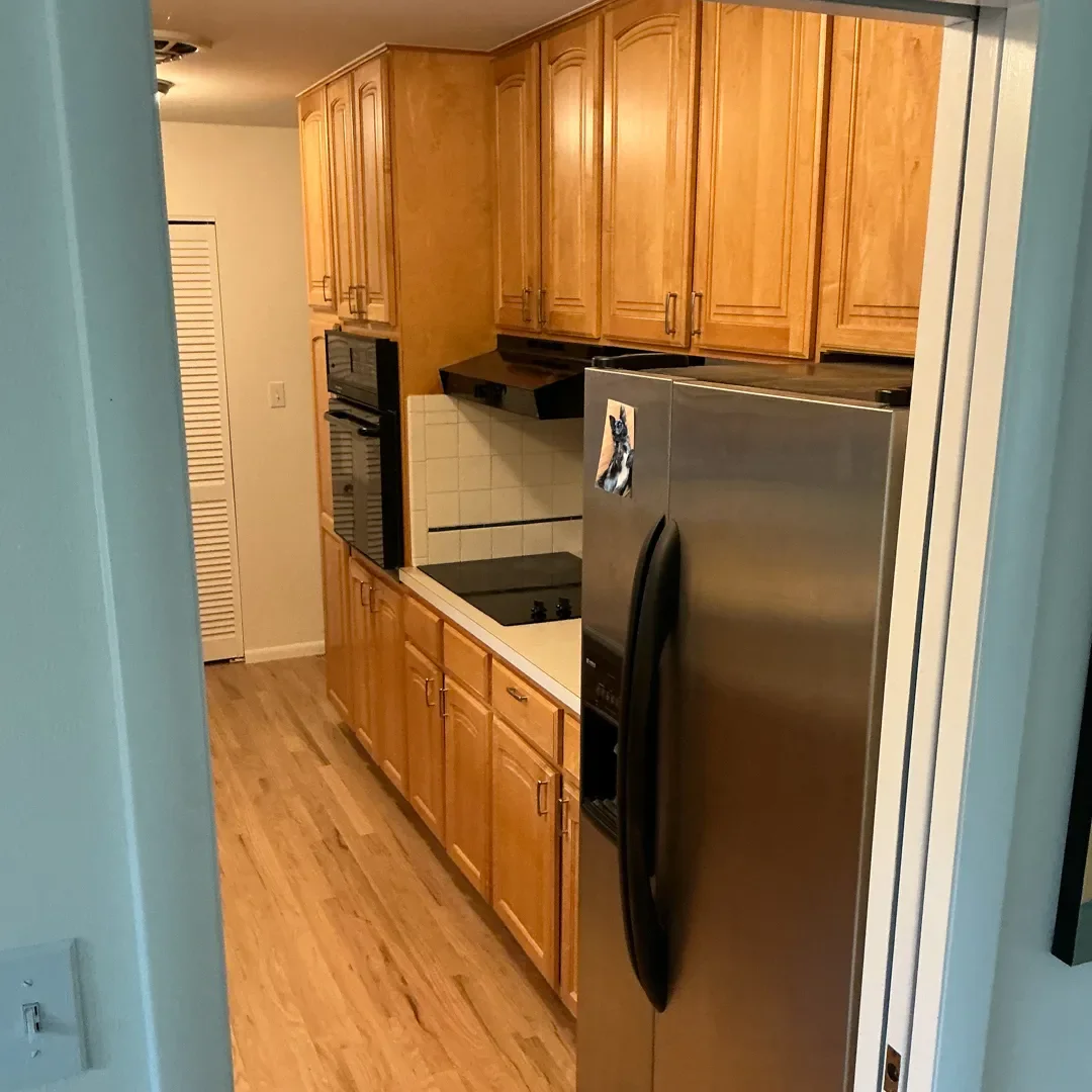 Kitchen in Longmont, CO awaiting renovation, showcasing cramped wall of cabinets, white tile backsplash, small black appliances, and limited countertop workspace