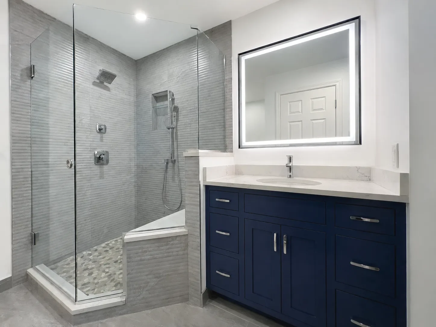 Modern bathroom remodel in Gunbarrel, CO with large full glass walk-in shower, shower bench, gray fluted shower tile, rainshower, wall niche, blue custom vanity, and LED mirror