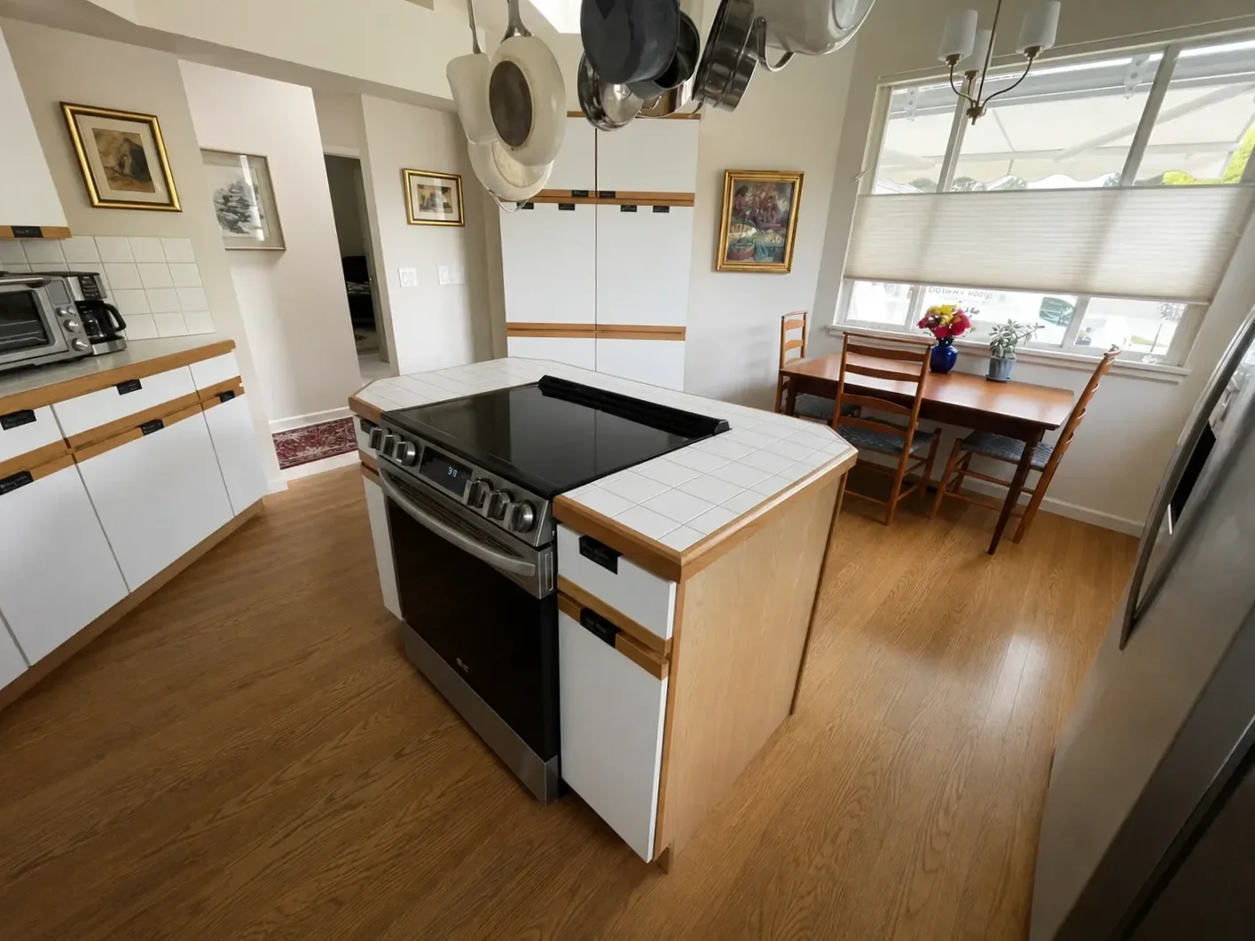 Large island with inset stove, hanging pot rack, and tile countertops in a Gunbarrel, CO kitchen before renovation