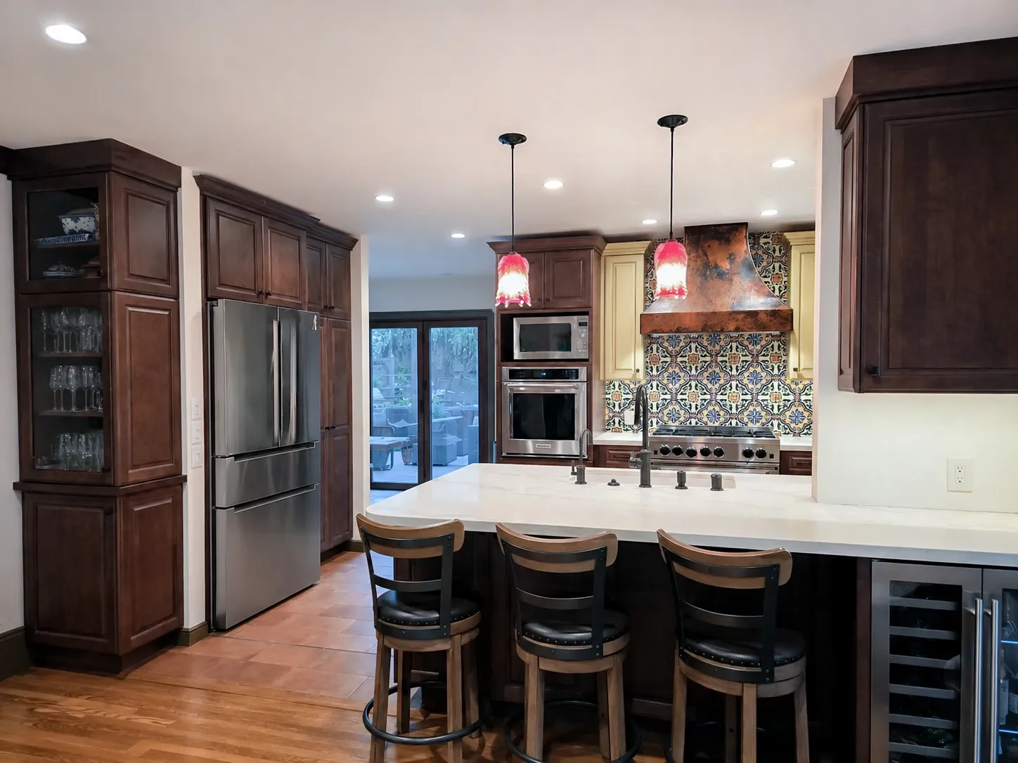 Modern kitchen with stainless steel appliances, colorful tiled backsplash, wooden cabinets, island with chairs, and pendant lighting.