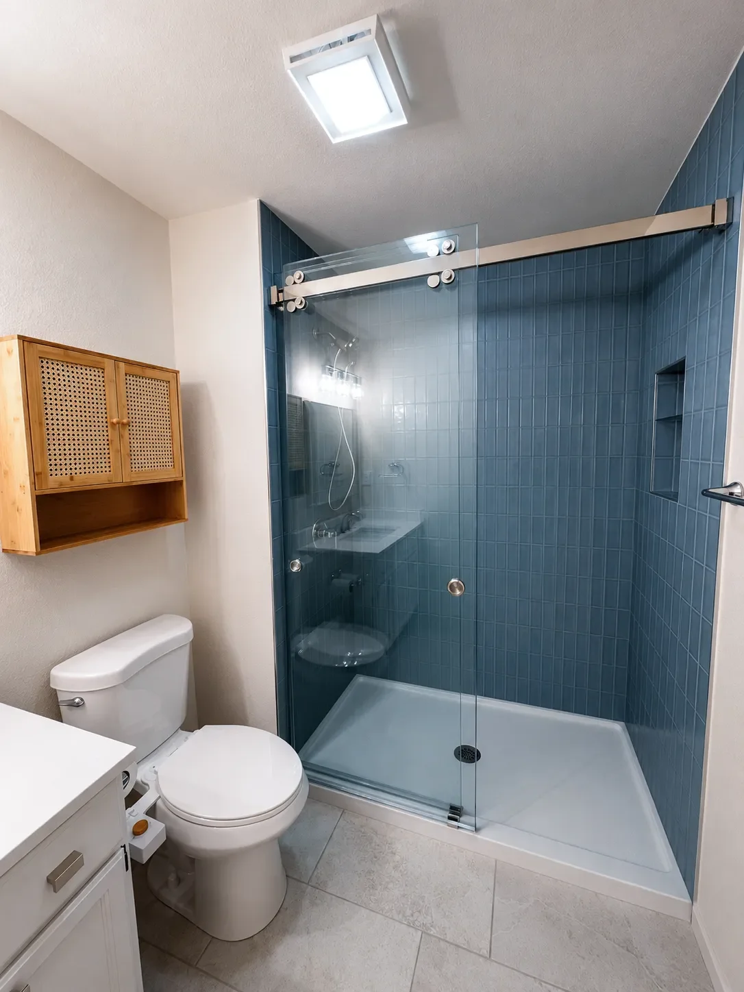 View of sliding glass walk-in shower with blue tile and shower niche in a newly renovated contemporary bathroom in Gunbarrel, CO