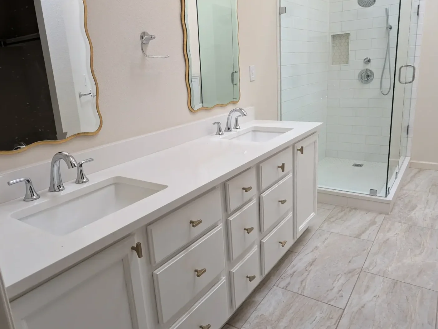 Before photo of master bathroom prior to renovation featuring basic white double vanity, narrow walk-in shower with white subway tiles, and gray tile floor in Gunbarrel, CO,
