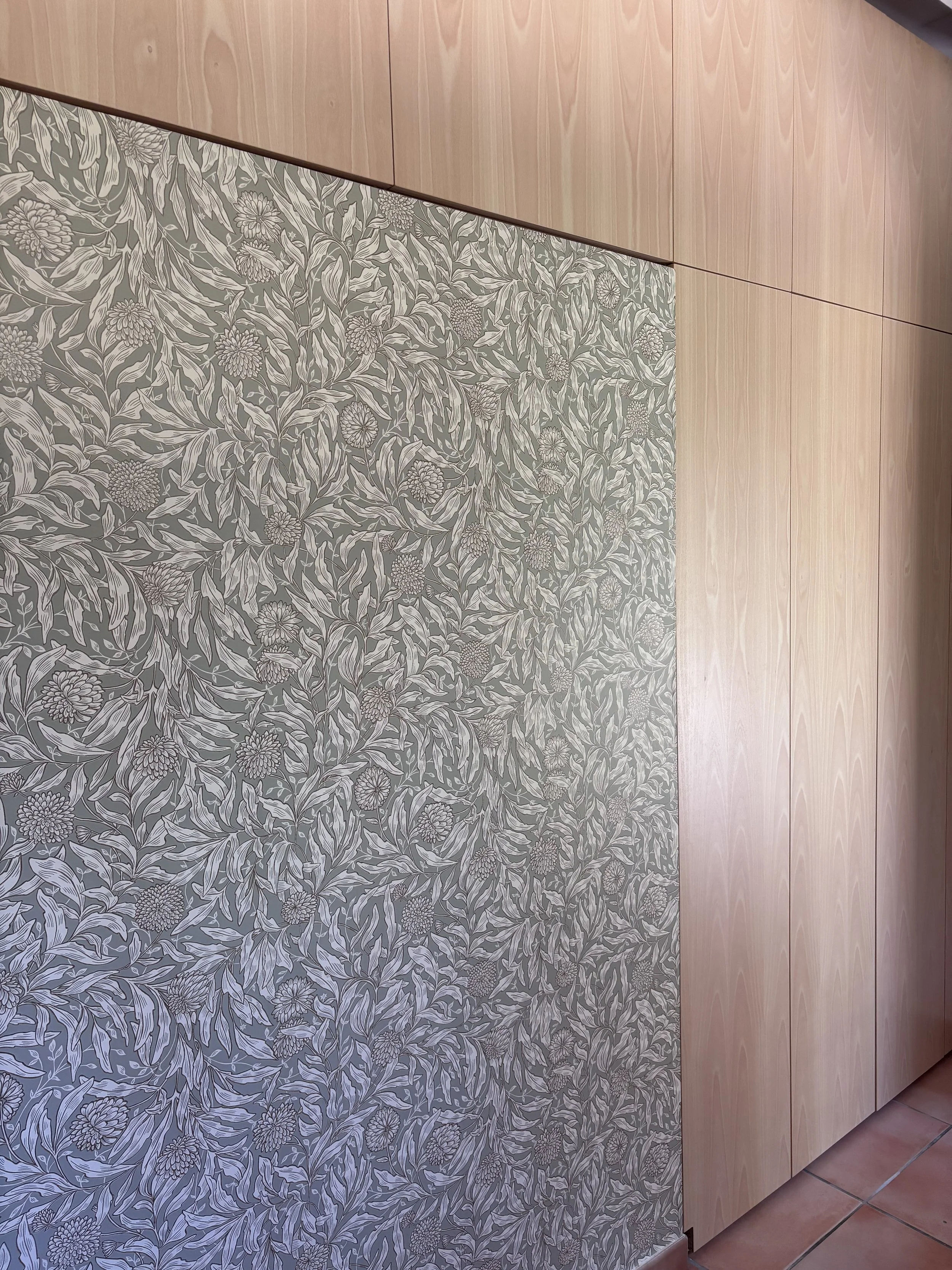 Un mur avec un papier peint floral gris et blanc et des panneaux en bois clair.