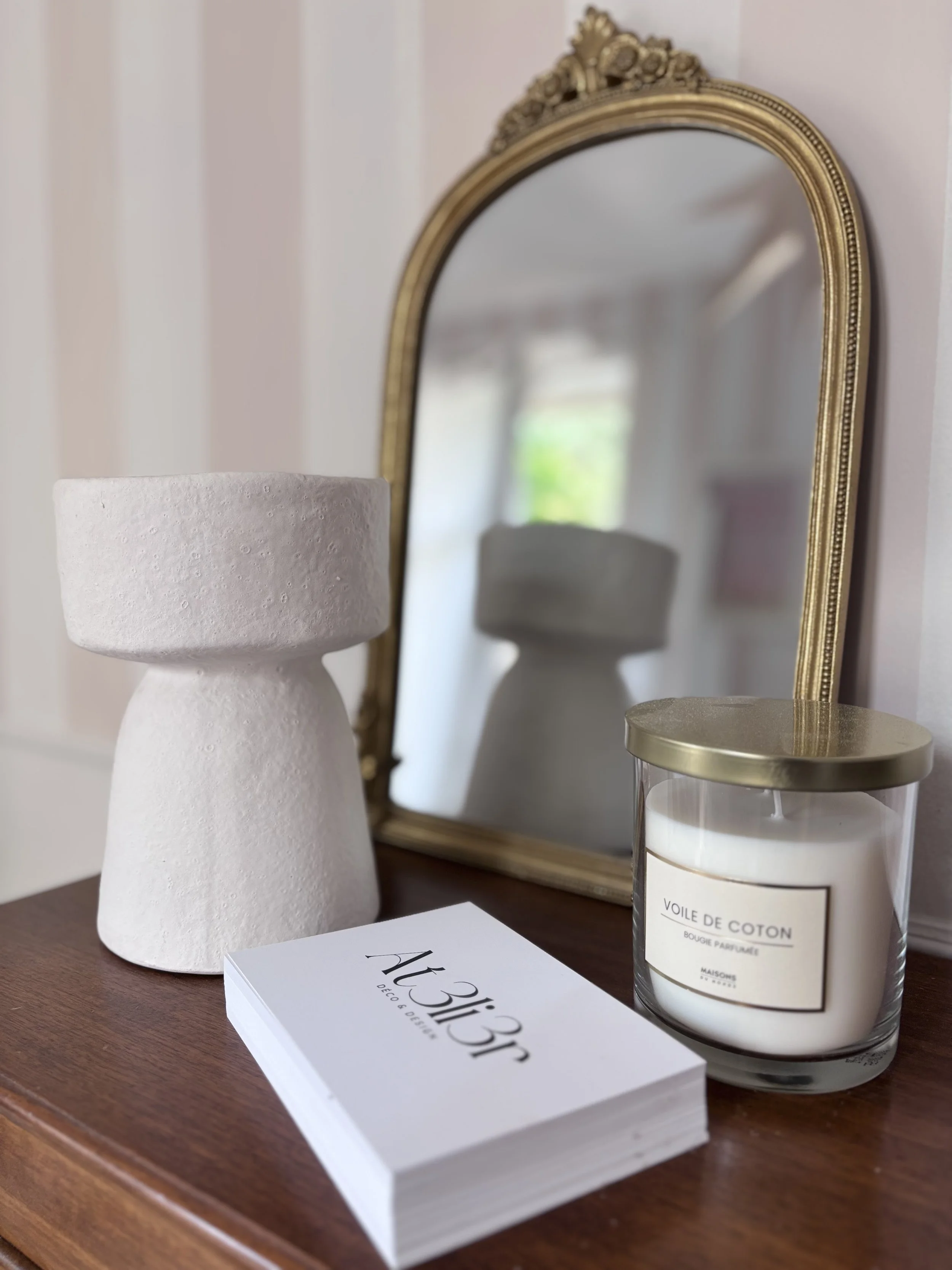 Cartes professionnelles sur piano, petits bibelots: miroir, vase et bougie. Papier peint rayé rose blanc