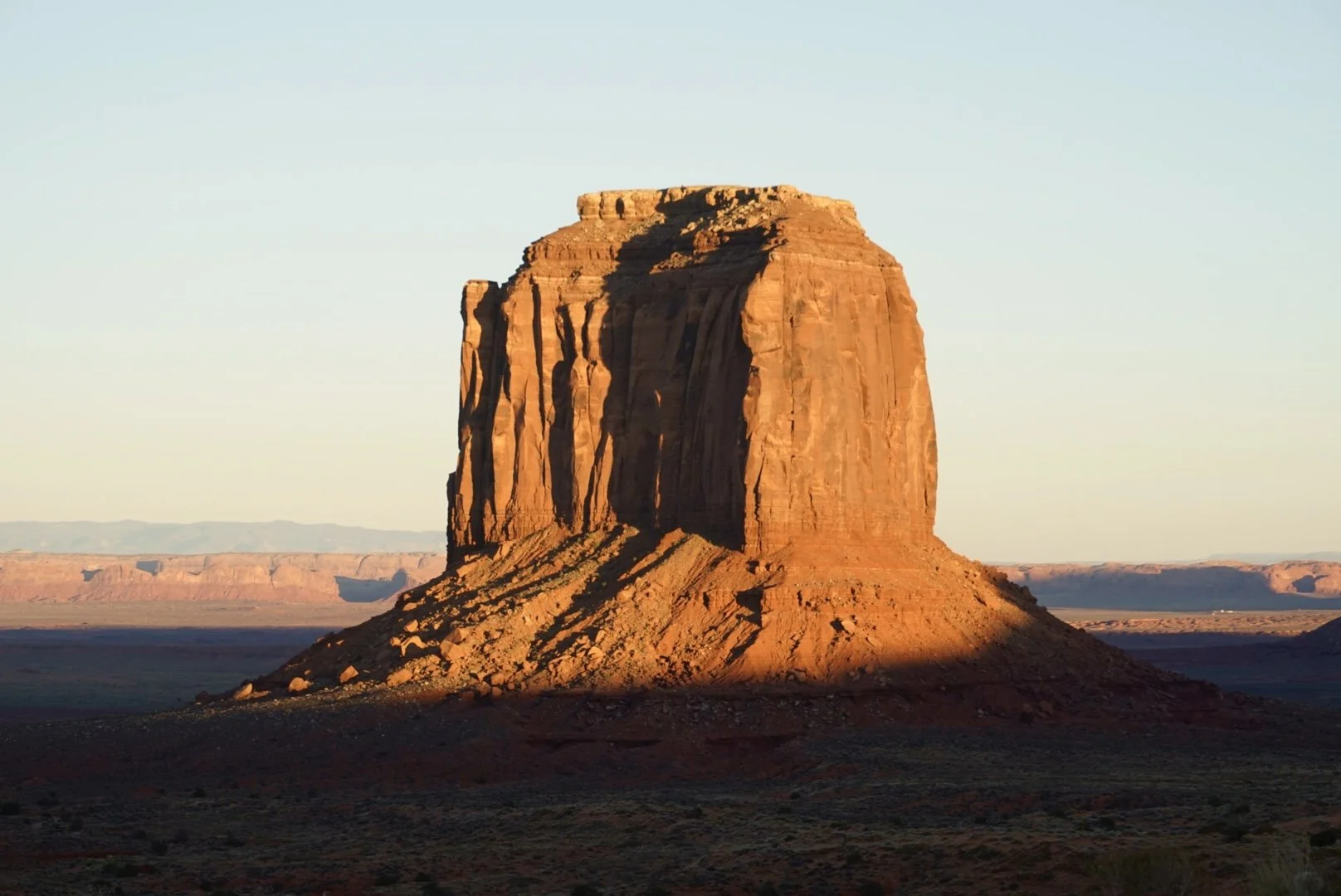 A large sandstone butte in Monument Valley, Arizona, landscape at sunset, with a clear sky and distant mesas.
