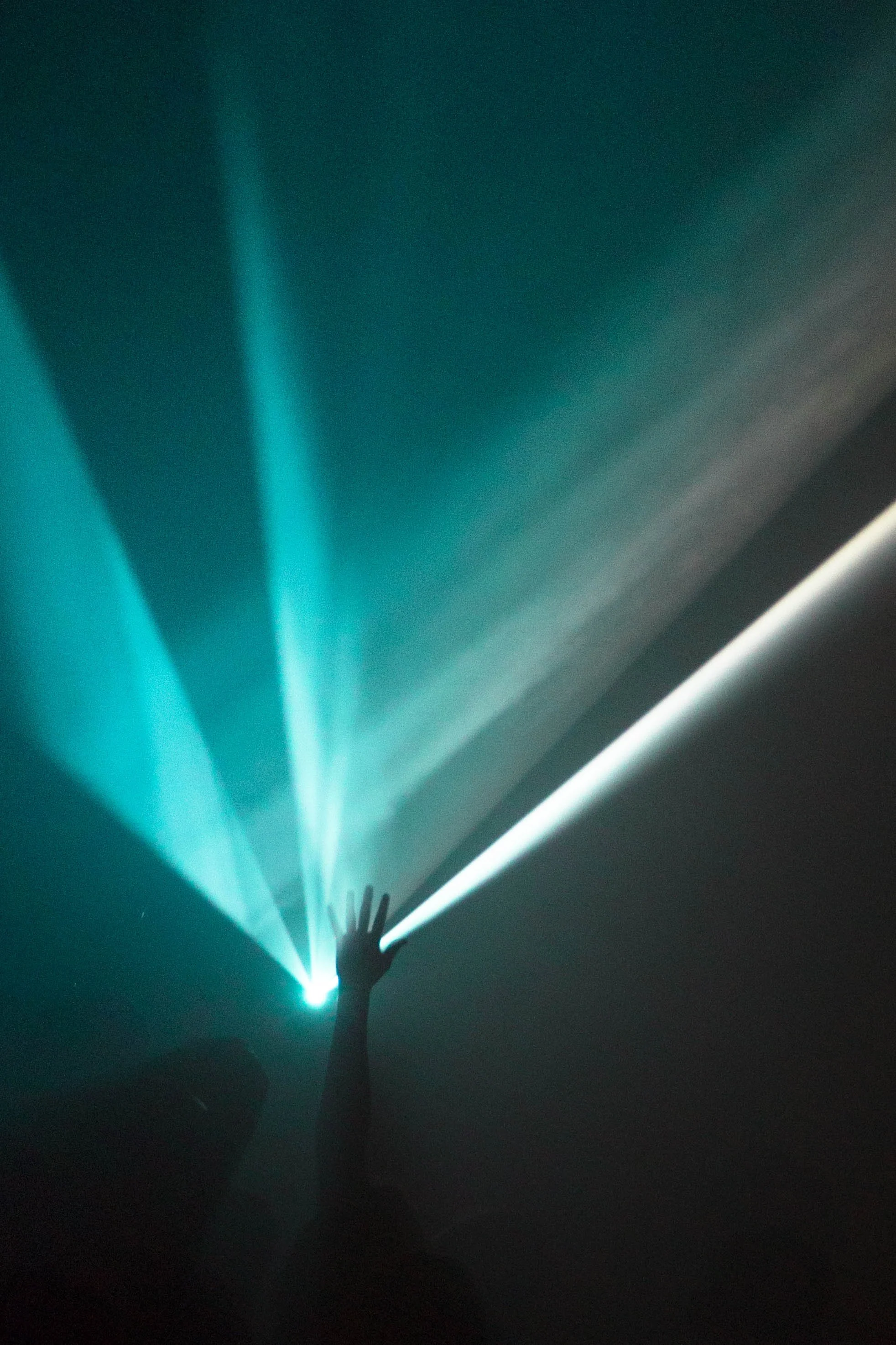 A person stands with their arm raised during a gig in London, making contact with the blue and white light into the dark space, creating a radiant display.