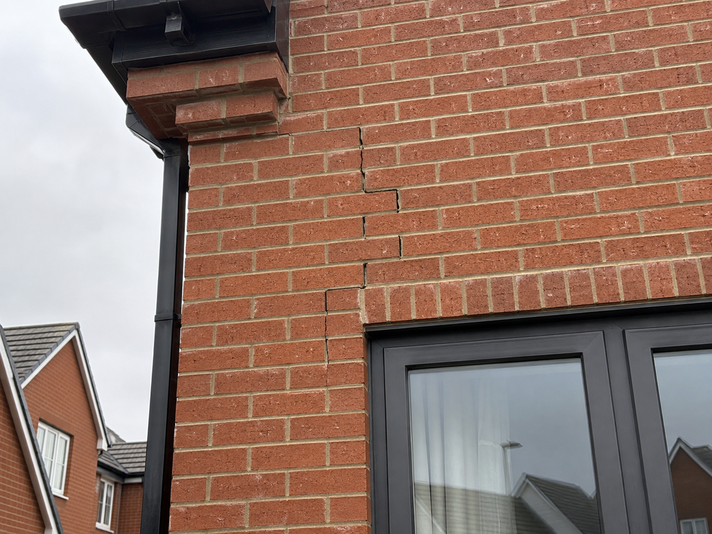 Brick house exterior with a large crack in the brick wall near the window.