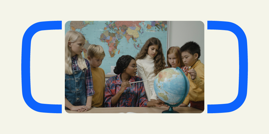 A teacher showing a globe to a group of children in a classroom with a world map on the wall.