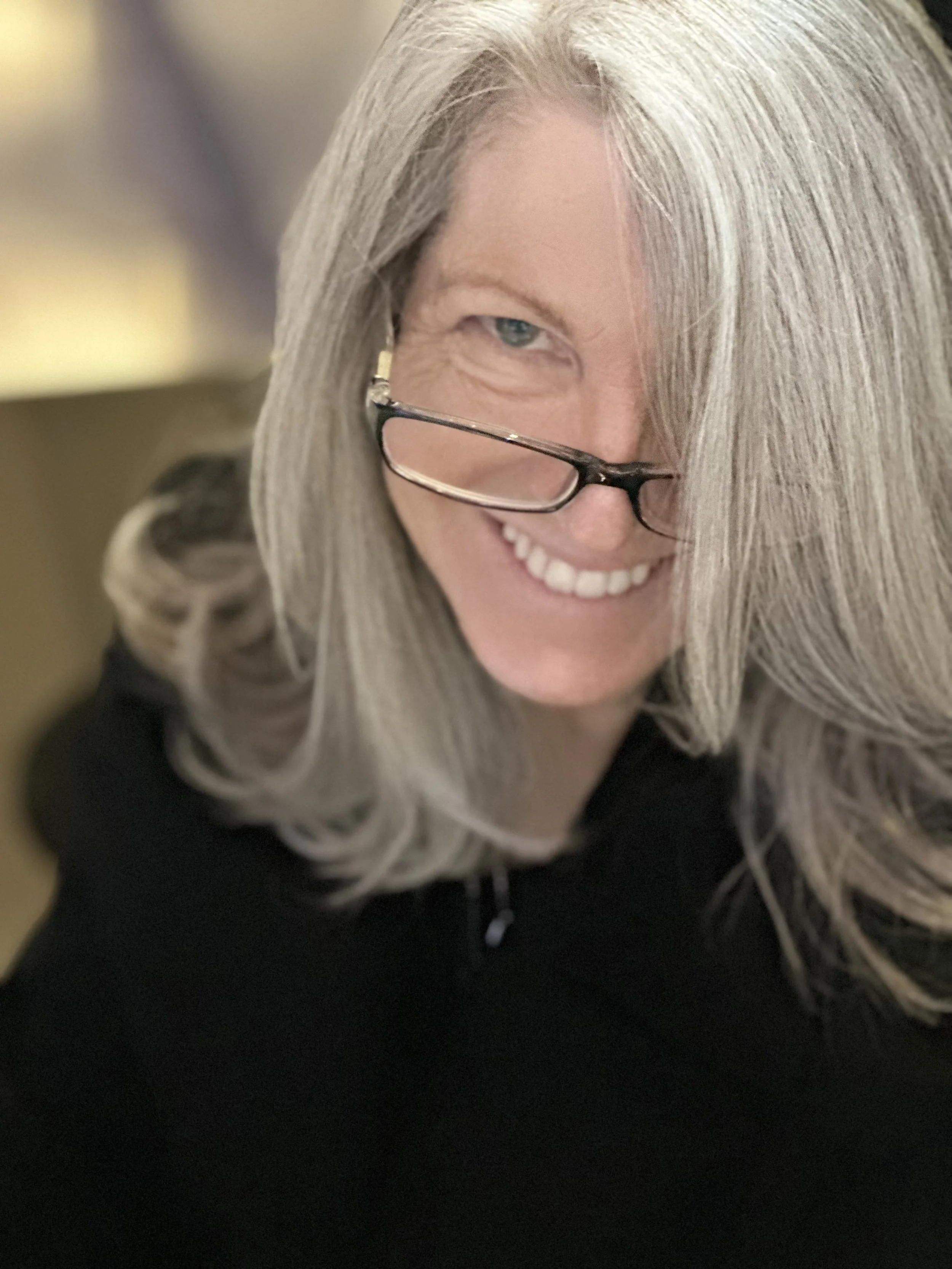 A smiling woman with gray hair, wearing glasses and a black top, looking at the camera.