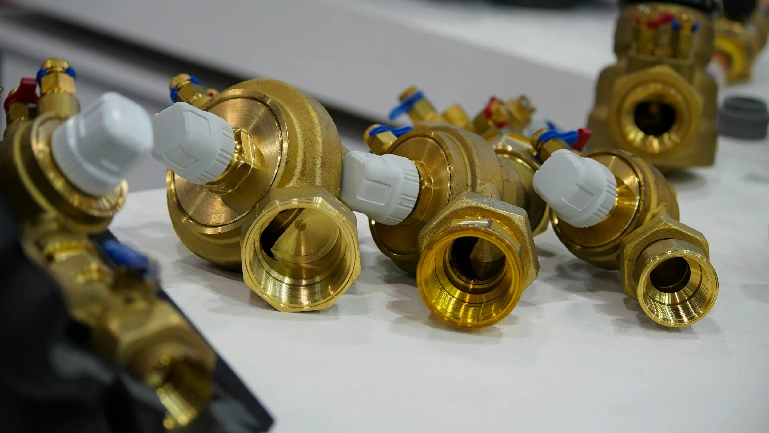 Multiple brass and white plastic plumbing valves and fittings scattered on a white surface.